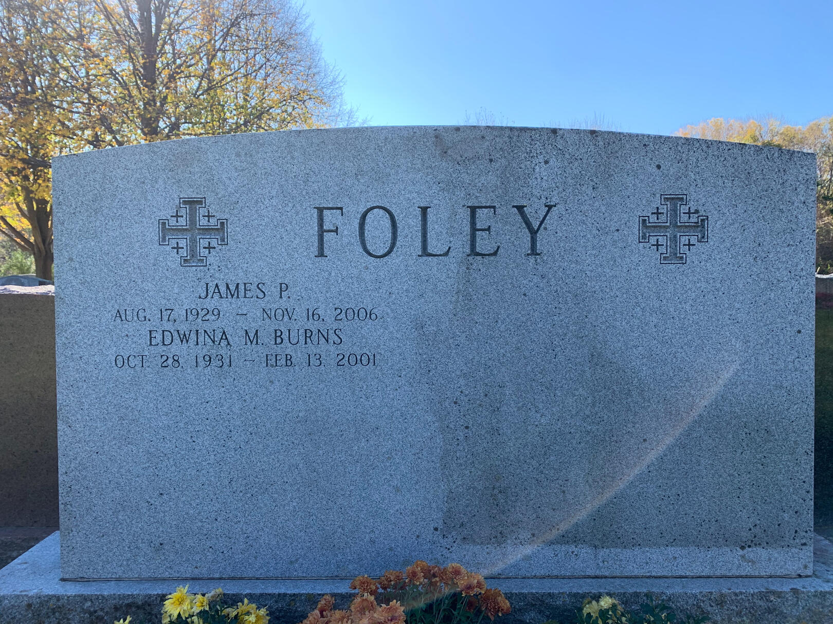 A clean granite headstone under a clear blue autumn sky with fall flower plantings at its base